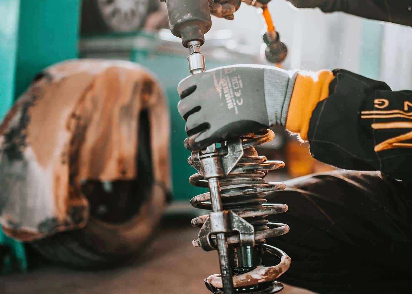 A mechanic working on the suspension of a raised car with a drill