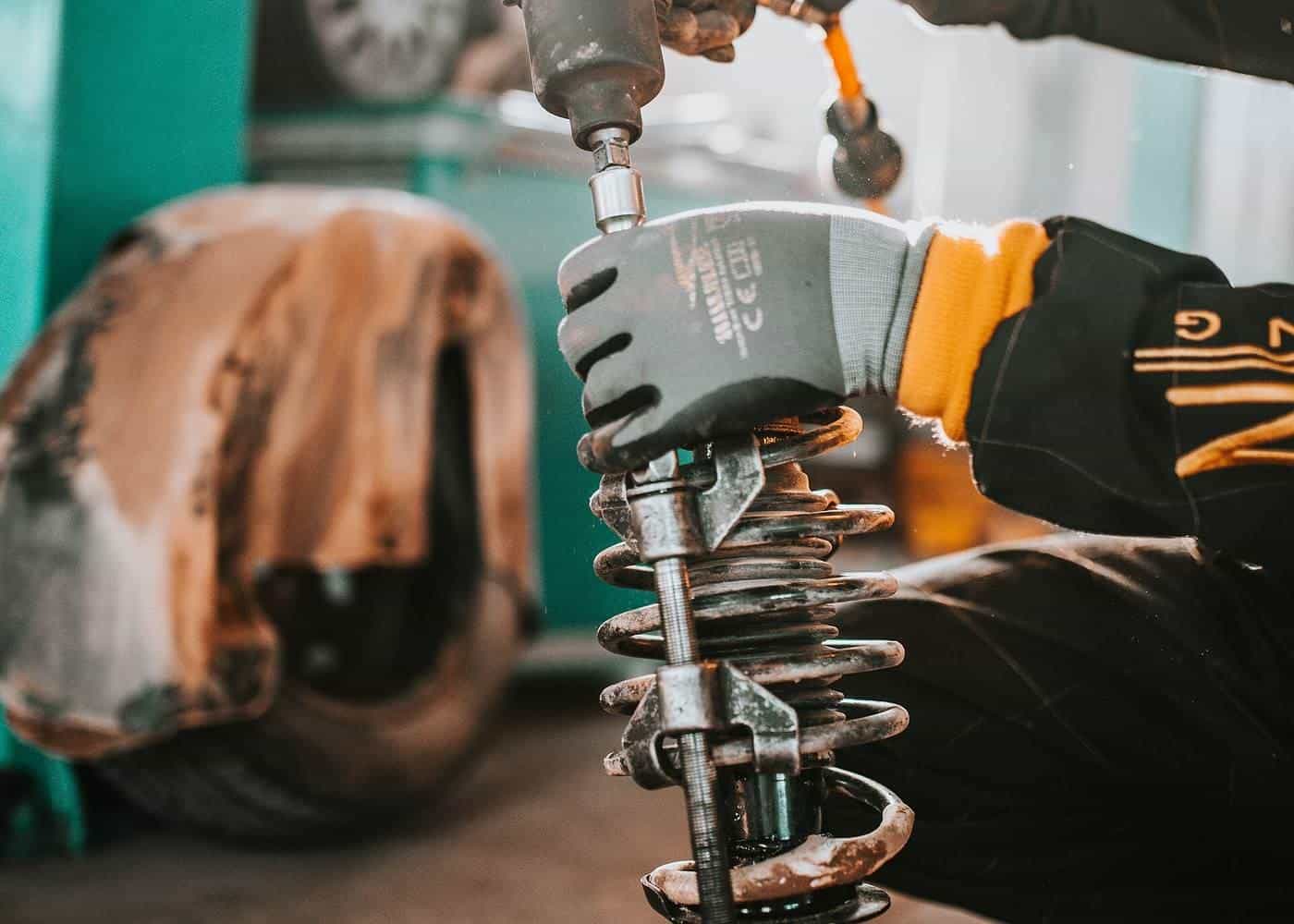 A mechanic working on the suspension of a raised car with a drill